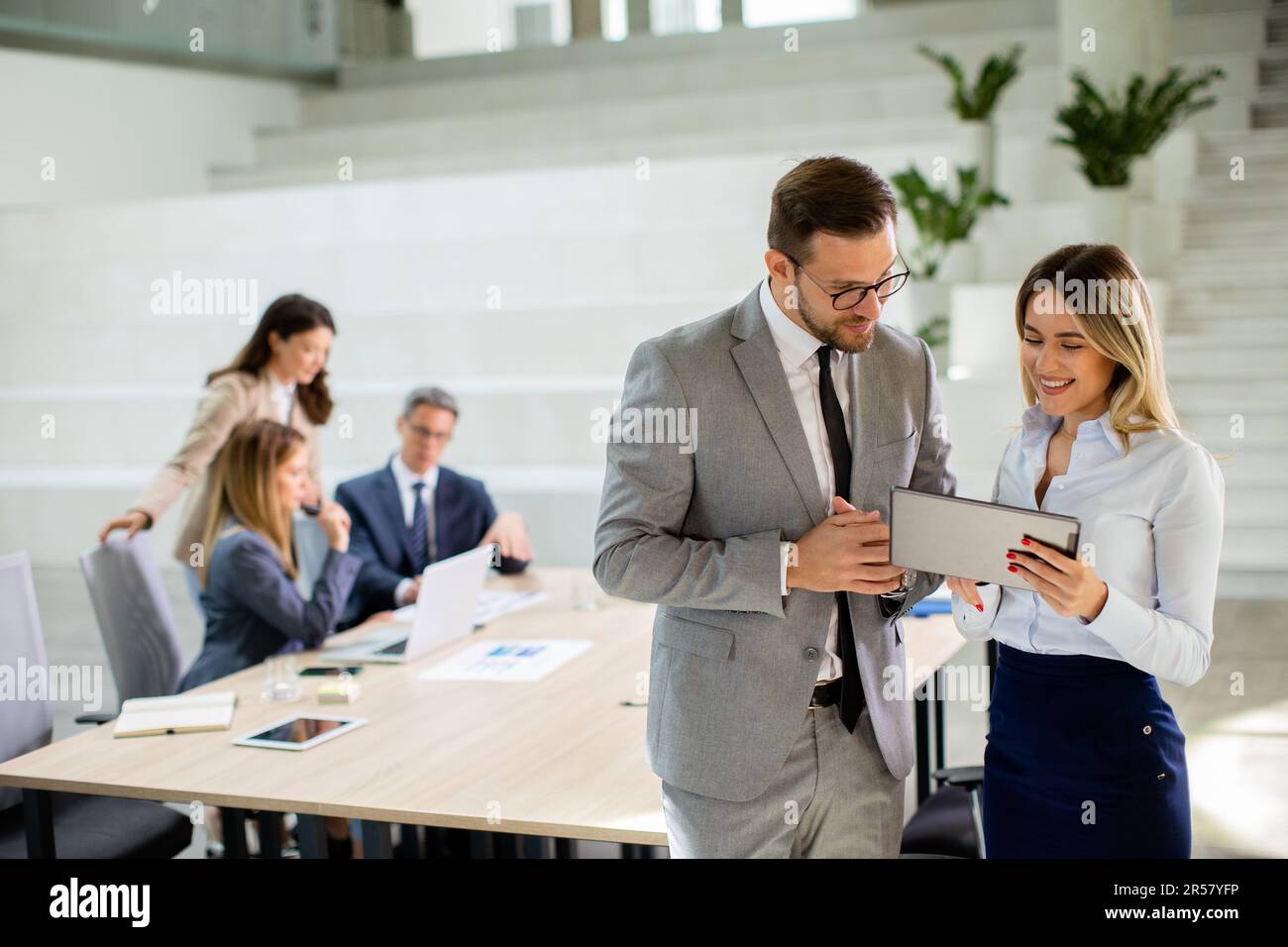 Attraktives junges Geschäftspaar, das sich die finanziellen Ergebnisse auf einem digitalen Tablet vor seinem Team im Büro ansieht Stockfoto
