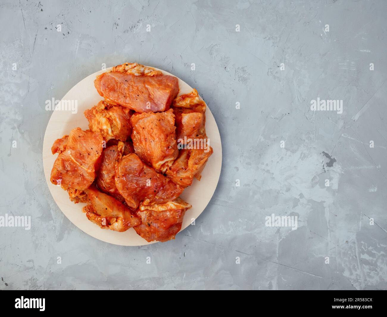 Roher truthahn in einer Marinade mit Gewürzen auf einem freundlichen Einwegteller. Mariniertes Hähnchen zum Grillen und grillen. Rohes gewürztes Fleisch für Shish Kebab auf Grau Stockfoto