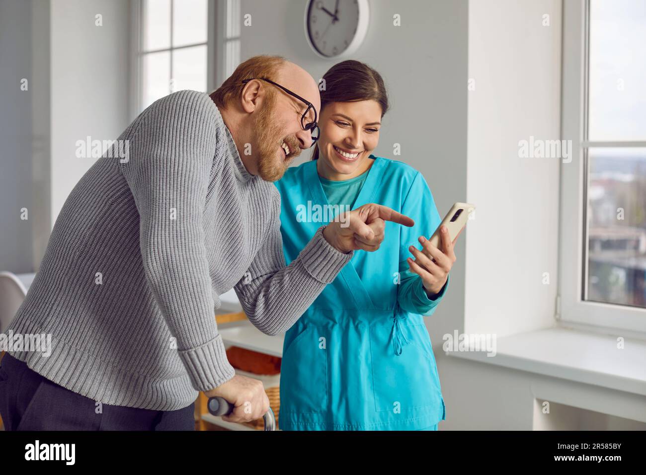 Ein rothaariger, bärtiger Mann mit einer fürsorglichen Krankenschwester lacht und amüsiert sich in einem Pflegeheim. Stockfoto