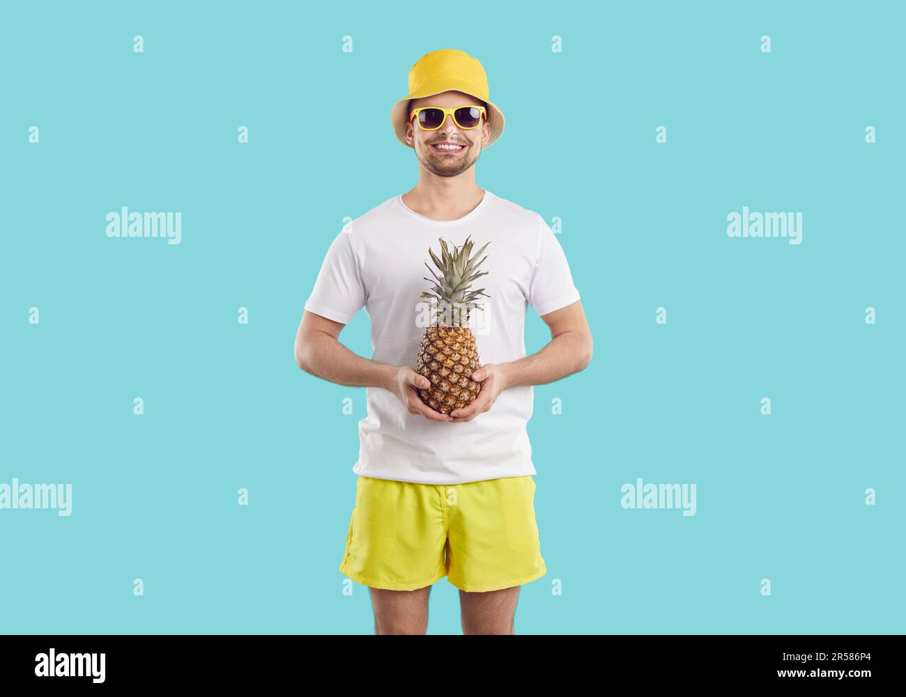 Fröhlicher, witziger, weißer Typ mit Ananas in den Händen, isoliert auf pastellfarbenem, hellblauem Hintergrund. Stockfoto