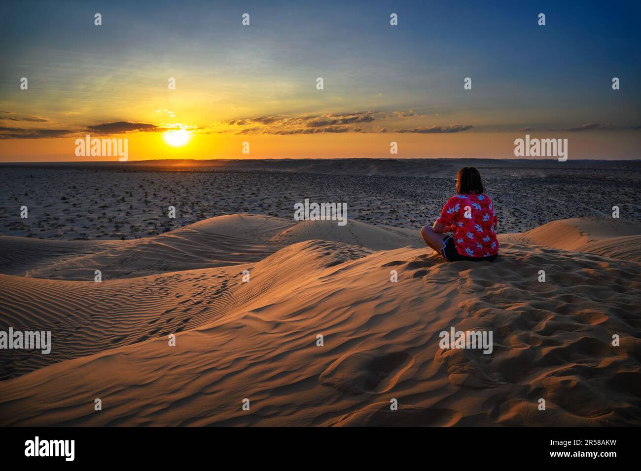 Eine Frau, die den Sonnenuntergang über den Sanddünen der arabischen Wüste in Oman beobachtet Stockfoto