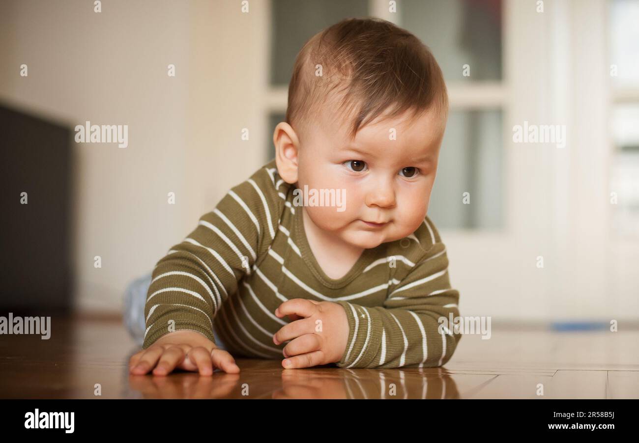 Der süße Junge krabbelt auf dem Hausboden herum, erkundet die Welt und lernt, sich zu bewegen. Liebe und Familiengefühle Stockfoto