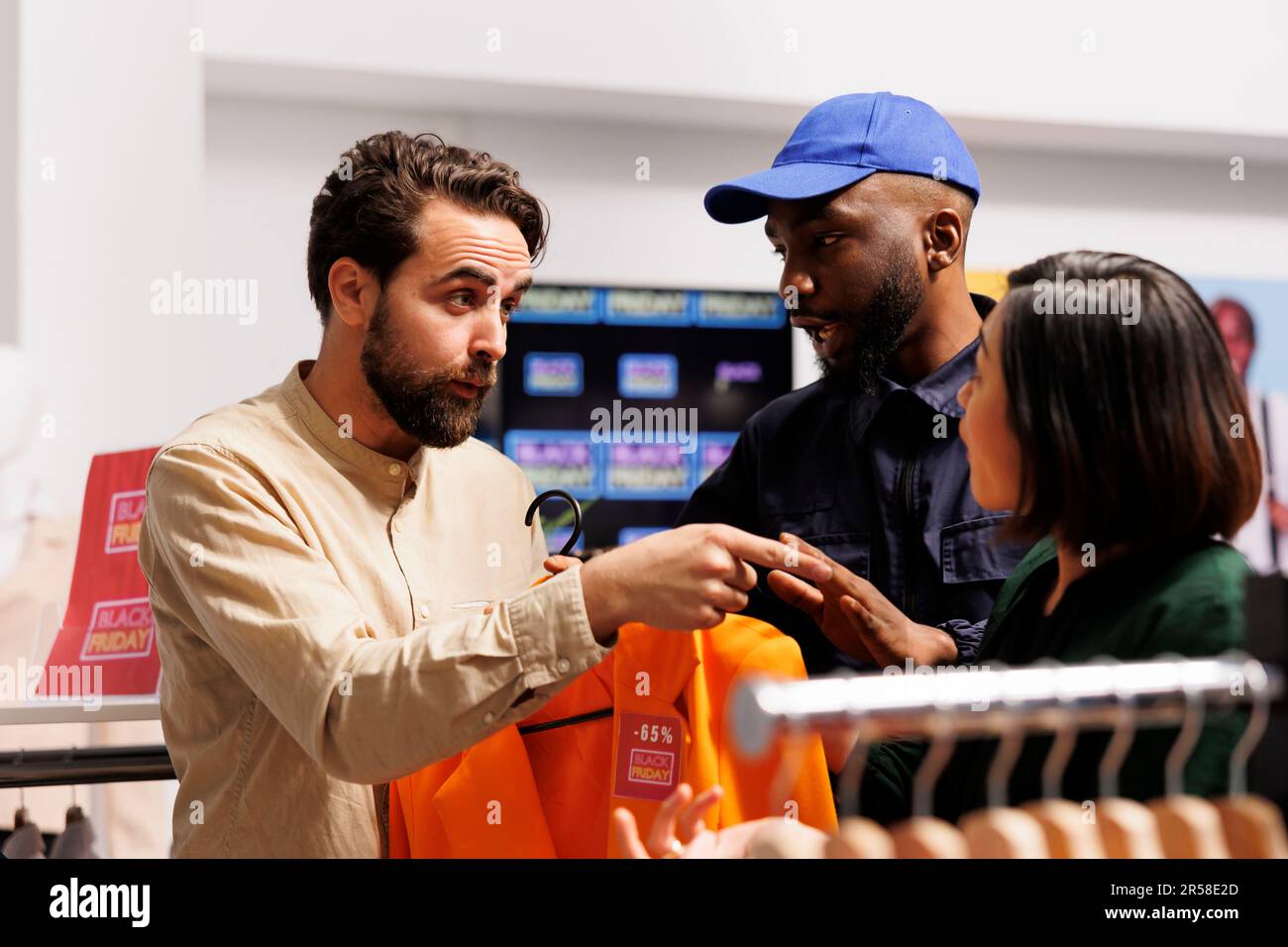 Verrückte Kunden, Mann und Frau, streiten um Schnäppchen im Einkaufszentrum. Ein afroamerikanischer Sicherheitsbeauftragter, der sich während des Black Friday-Verkaufs mit aggressiven Käufern im Bekleidungsgeschäft auseinandersetzt Stockfoto