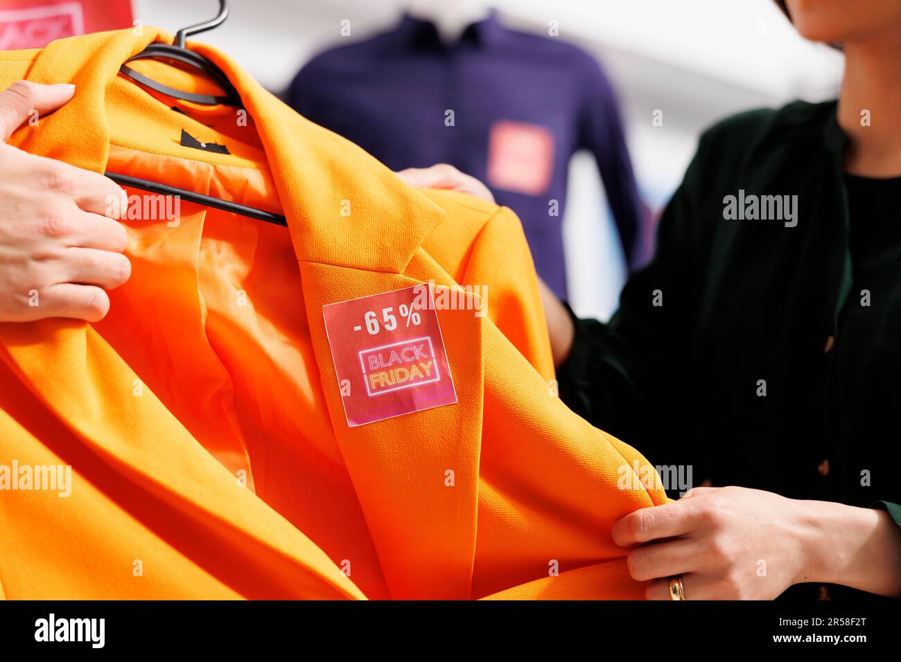 Nahaufnahme von zwei Käufern, die einen Kleidungsgegenstand mit rotem Preisschild in verschiedenen Richtungen halten. Leute, die im Bekleidungsgeschäft stehen und sich während des Black Friday-Einkaufs streiten Stockfoto