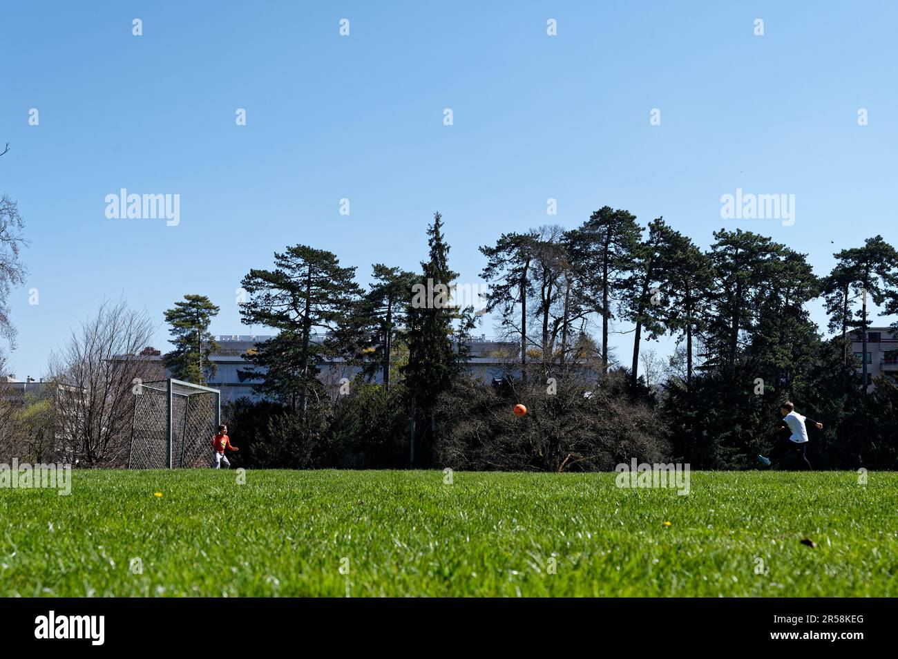 Zwei Kinder spielen Fußball im Alfred Bertrand Park. Der Junge tritt einen Fußball in Richtung Torwart. Stockfoto
