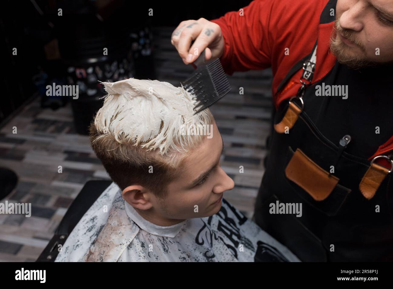 Die Hand eines professionellen Friseurs mit Kammaufsatz prüft den Grad der Färbung des Haares des Kunden im Friseur bei der Arbeit. Stockfoto