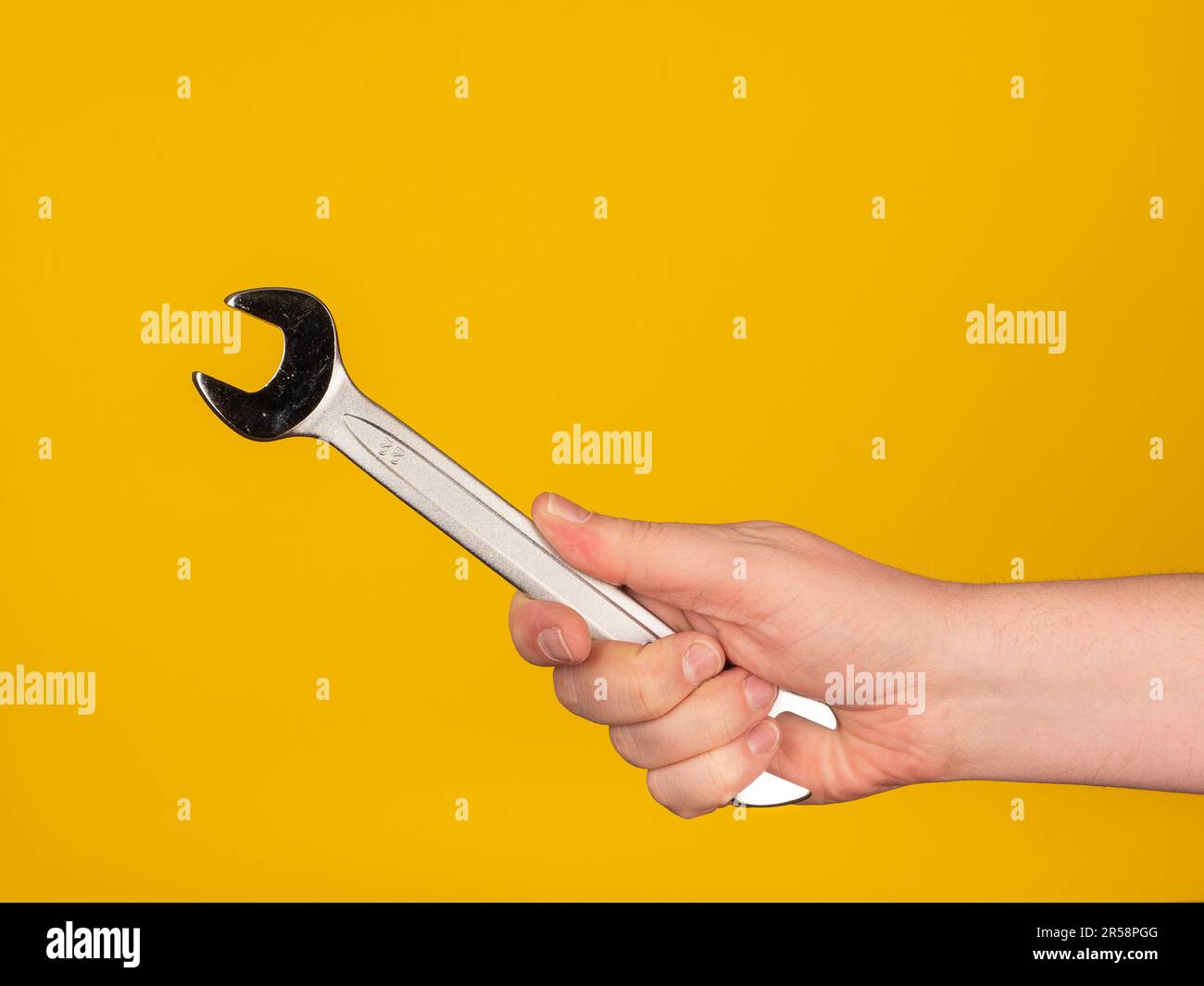 Eine Hand hält einen Maulschlüssel. Kein Gesicht, gelber Hintergrund. Stockfoto