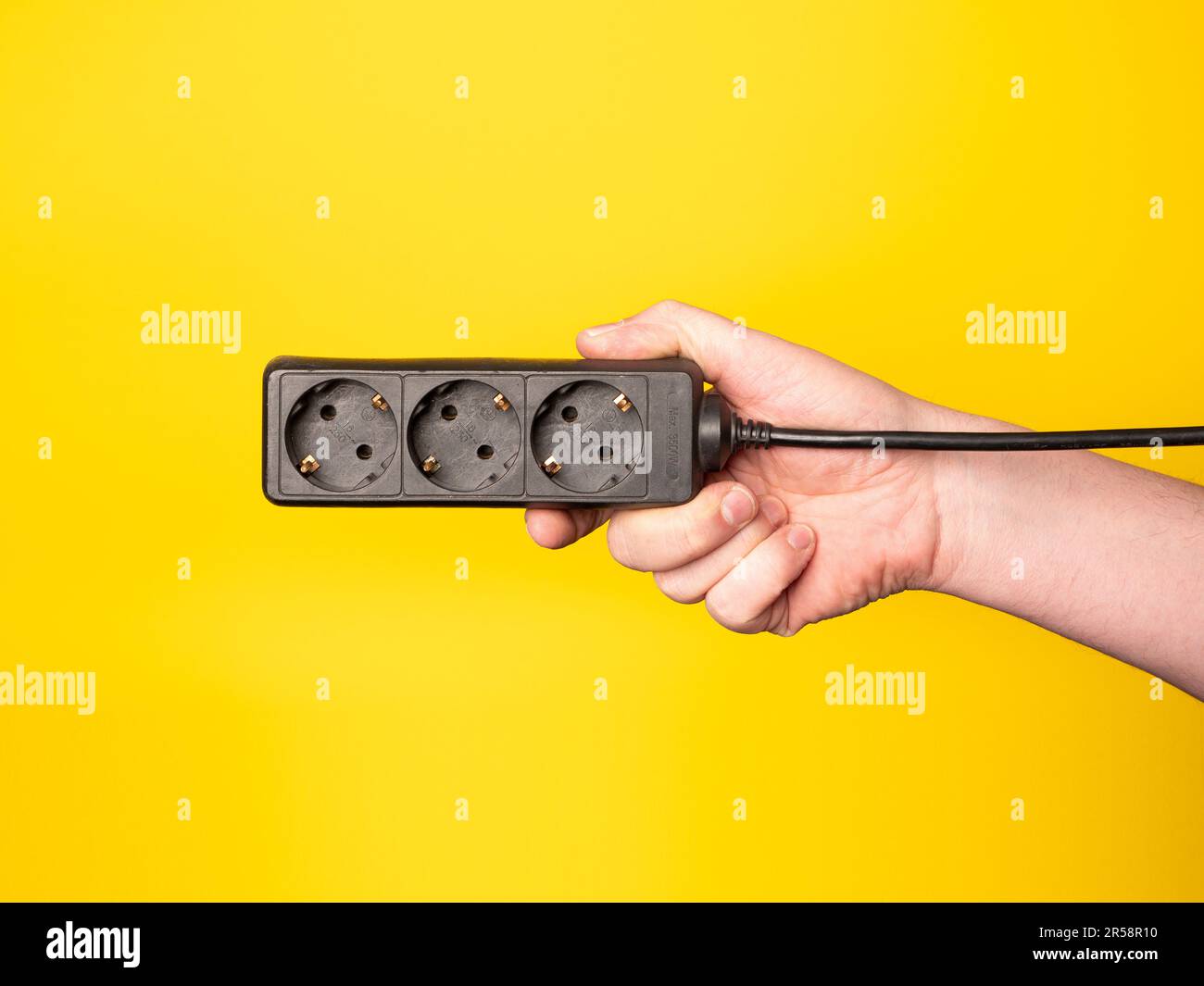Eine Hand hält eine Steckdosenleiste. Kein Gesicht, gelber Hintergrund. Stockfoto
