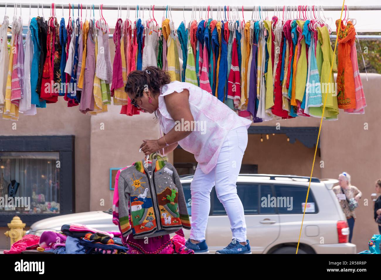 Eine Verkäuferin wacht auf, wenn sie ihren Stand für den Tag bereitstellt, in dem importierte Kleidung aufgehängt wird, wahrscheinlich aus Mexiko oder Mittelamerika – Santa Fe, New Mexico, USA Stockfoto