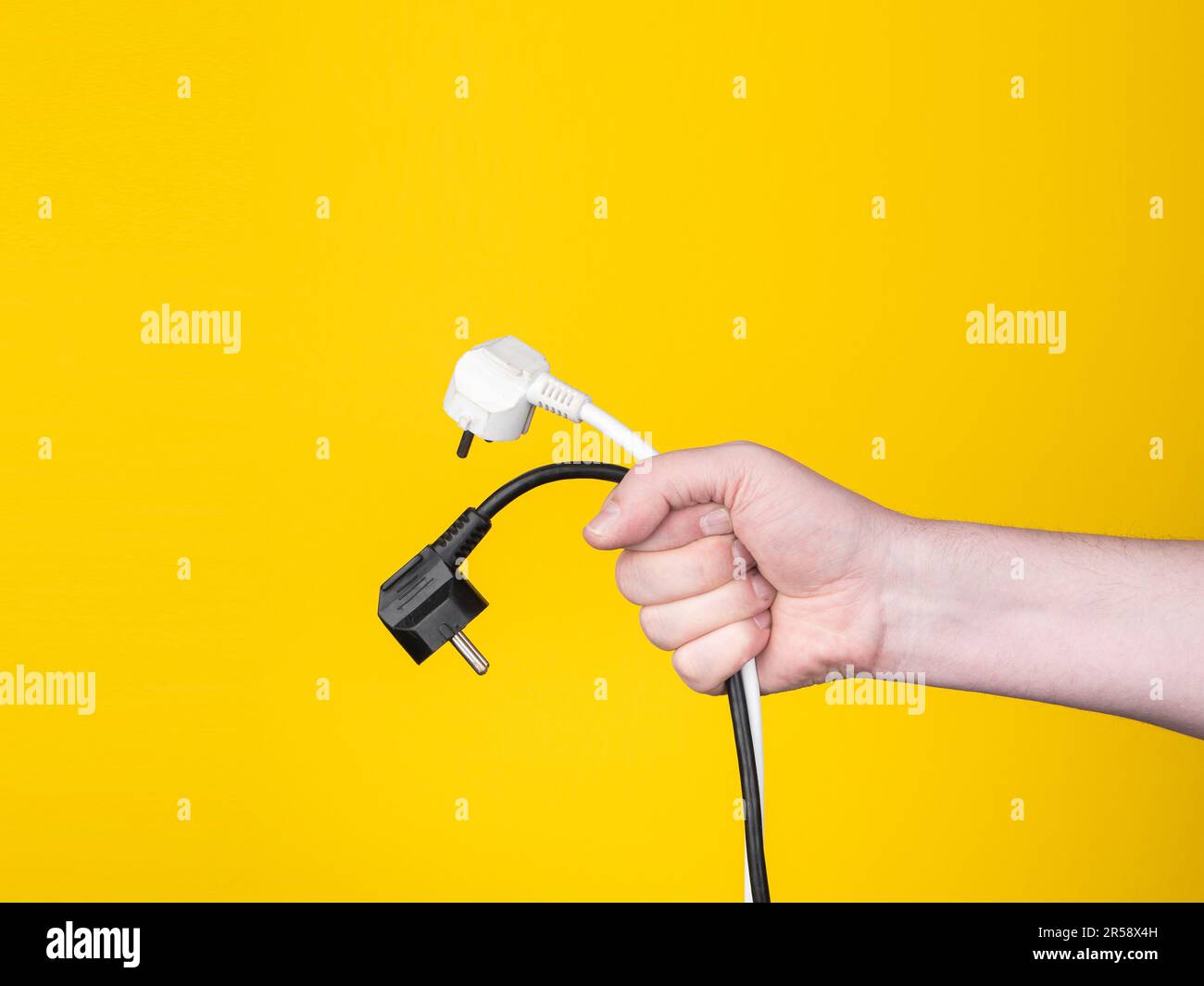 Eine Hand hält einen Stecker, an dem ein schwarzes Kabel befestigt ist. Kein Gesicht, gelber Hintergrund. Stockfoto Eine Hand hält einen Stecker, an dem ein schwarzes Kabel befestigt ist. Kein Gesicht, gelber Hintergrund. Stockfoto