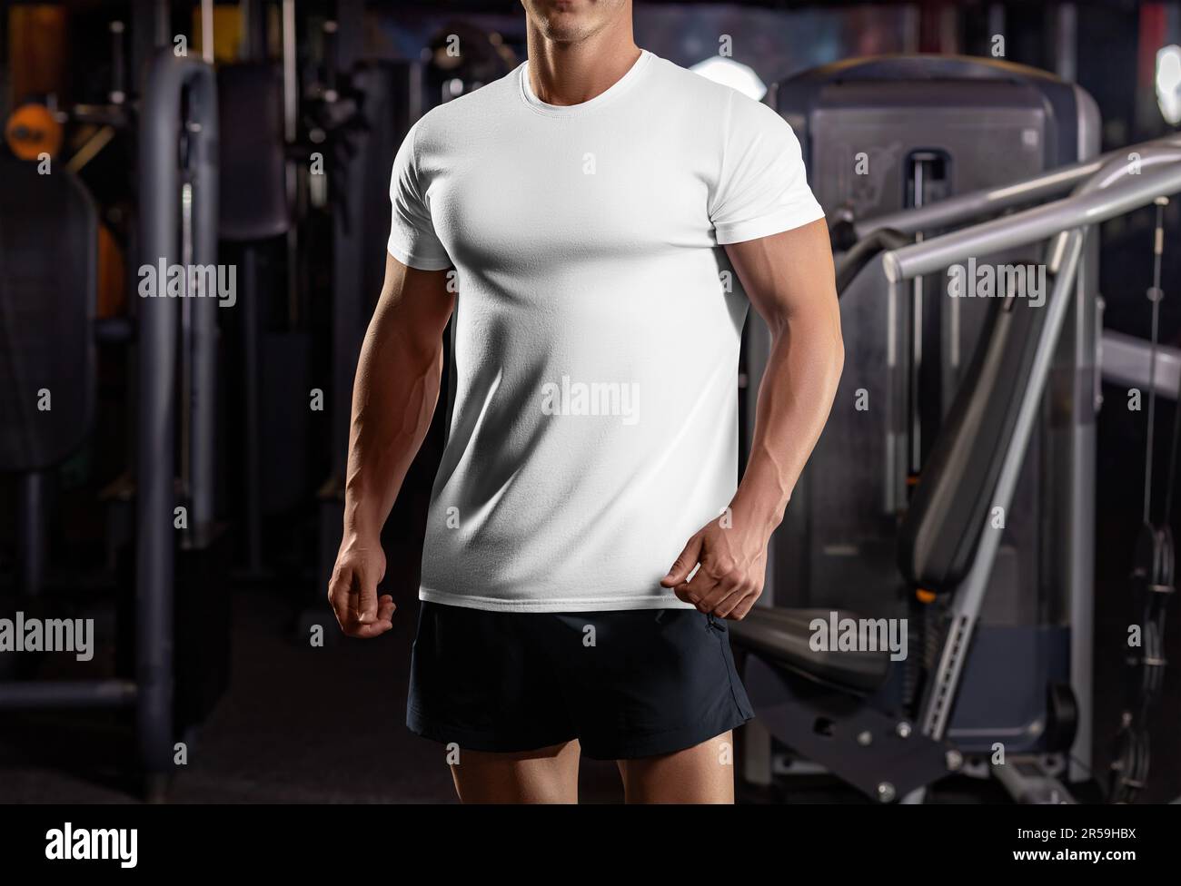 Modell eines weißen Sport-T-Shirts auf einem muskulösen Kerl im Fitnessstudio, bequeme Kleidung fürs Training, Platz für Design, Vorderansicht. Kleidungsvorlage auf einem Stockfoto