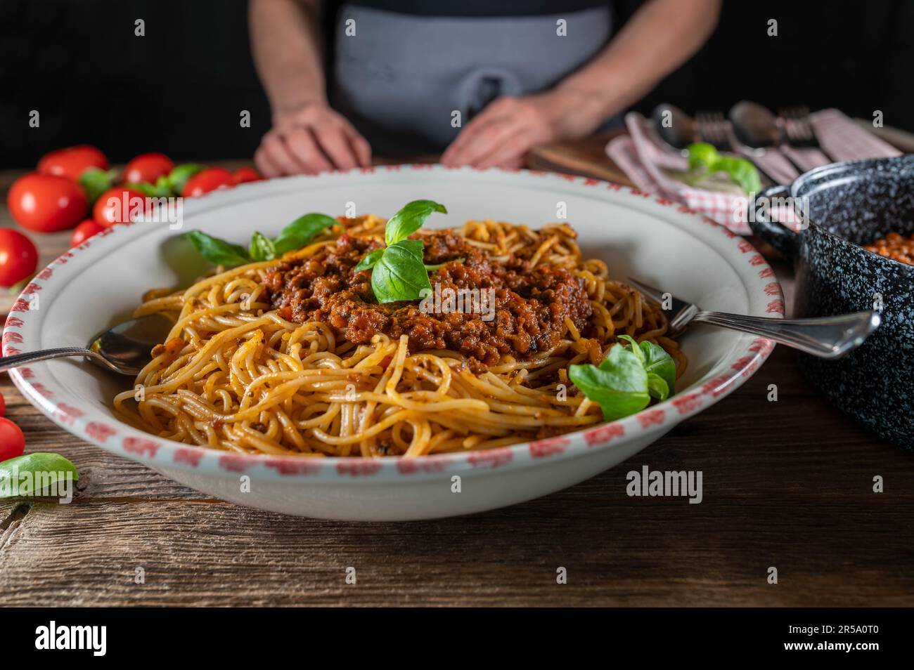 Frau, die eine große Nudelschüssel mit Spaghetti Bolognese auf rustikalem Holztisch hält oder serviert Stockfoto