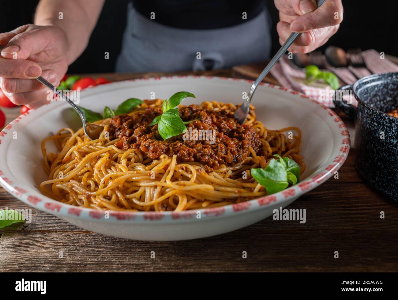 Eine Frau mit Schürze rührt Spaghetti mit Ragu alla Bolognese in einer großen Nudelschüssel auf einem Holztisch Stockfoto