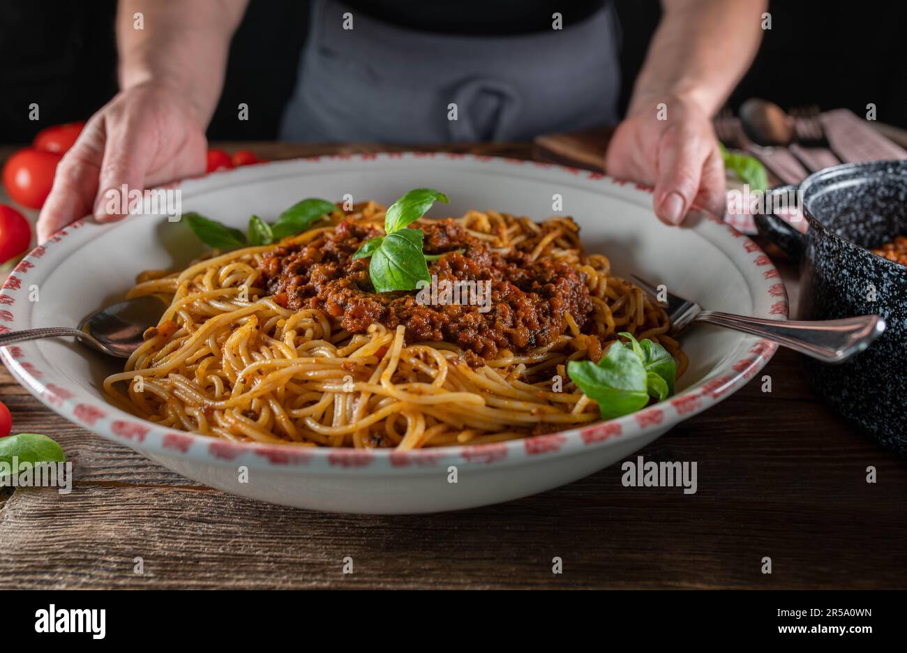 Frau, die eine große Nudelschüssel mit Spaghetti Bolognese auf rustikalem Holztisch hält oder serviert Stockfoto
