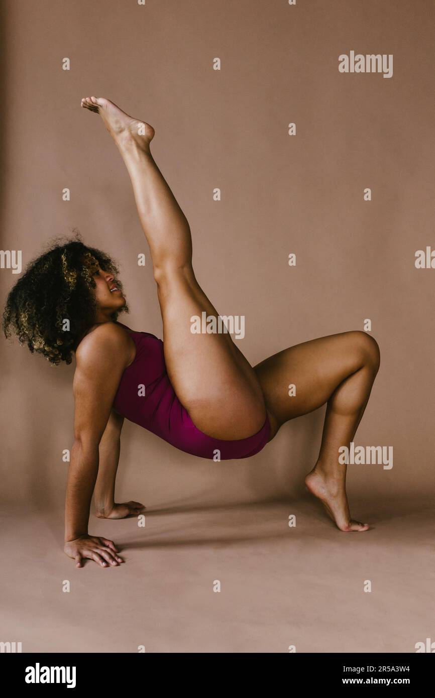 Tänzerin, die im Studio Beine hebt, mit lockigen Haaren, Körperbewegungen Stockfoto