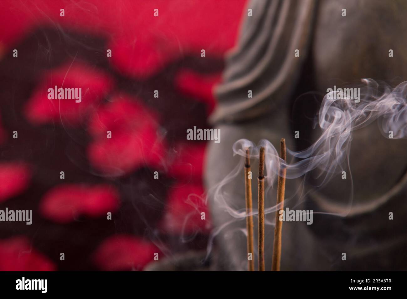 Buddha mit Räucherstäbchen unter Blütenblättern, Detail Stockfoto