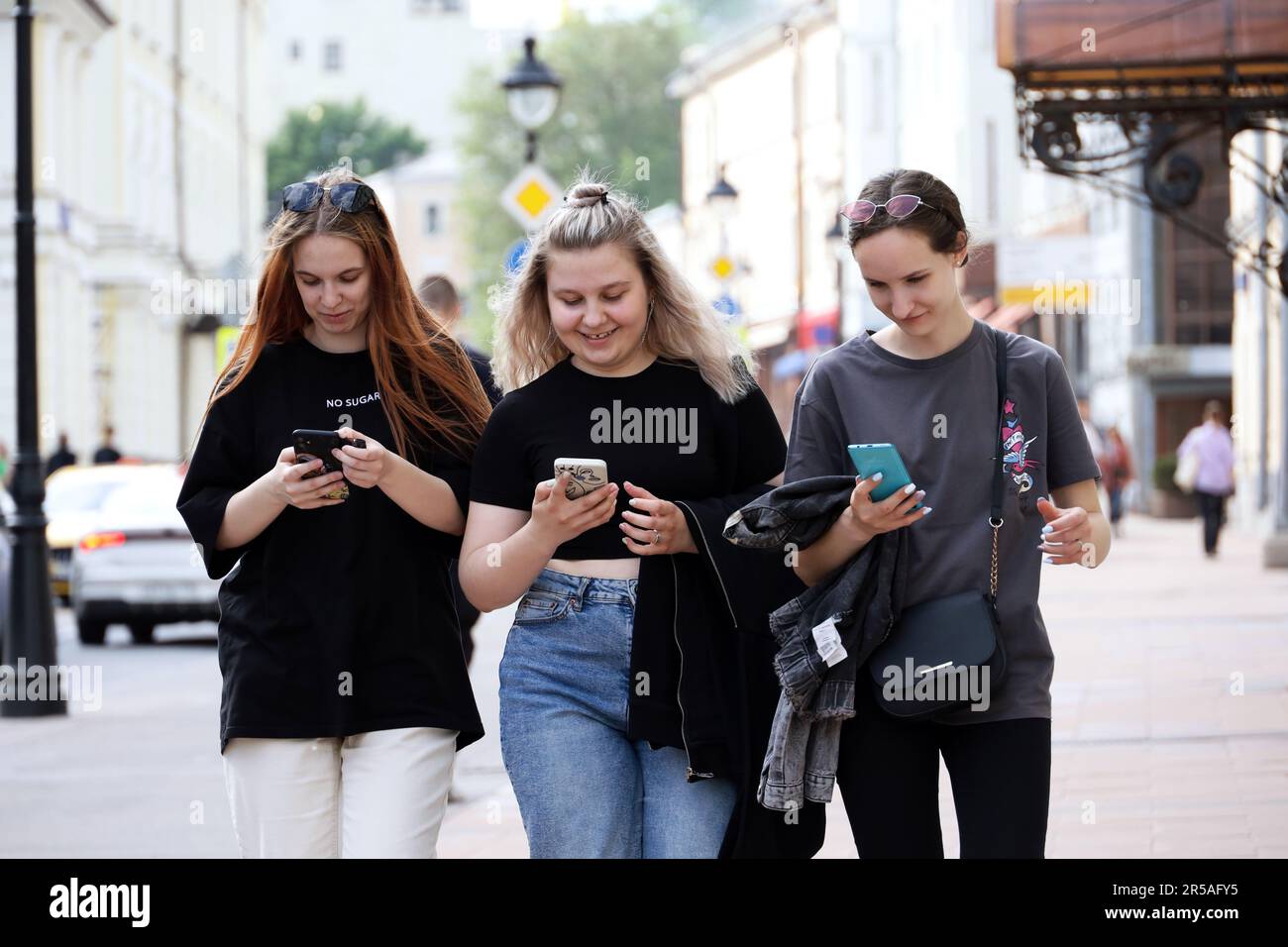 Glückliche Menschen, die Smartphones auf der Straße benutzen. Drei lächelnde Mädchen laufen mit Handys in der Hand Stockfoto