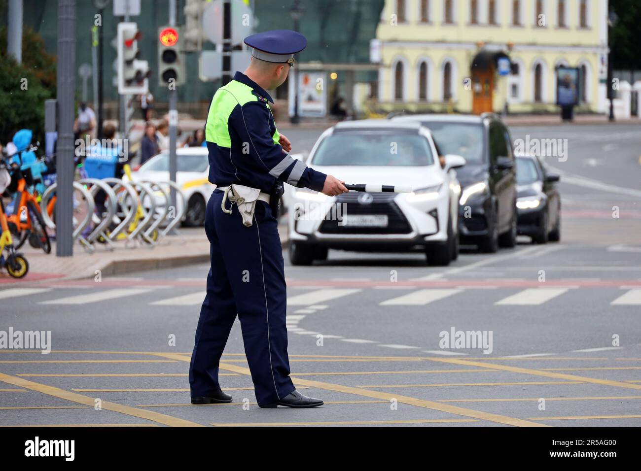Ein Verkehrspolizist steht mit einem Stab auf einer Straße vor dem Hintergrund eines Autos. Ein Polizist patrouilliert auf der Straße Stockfoto