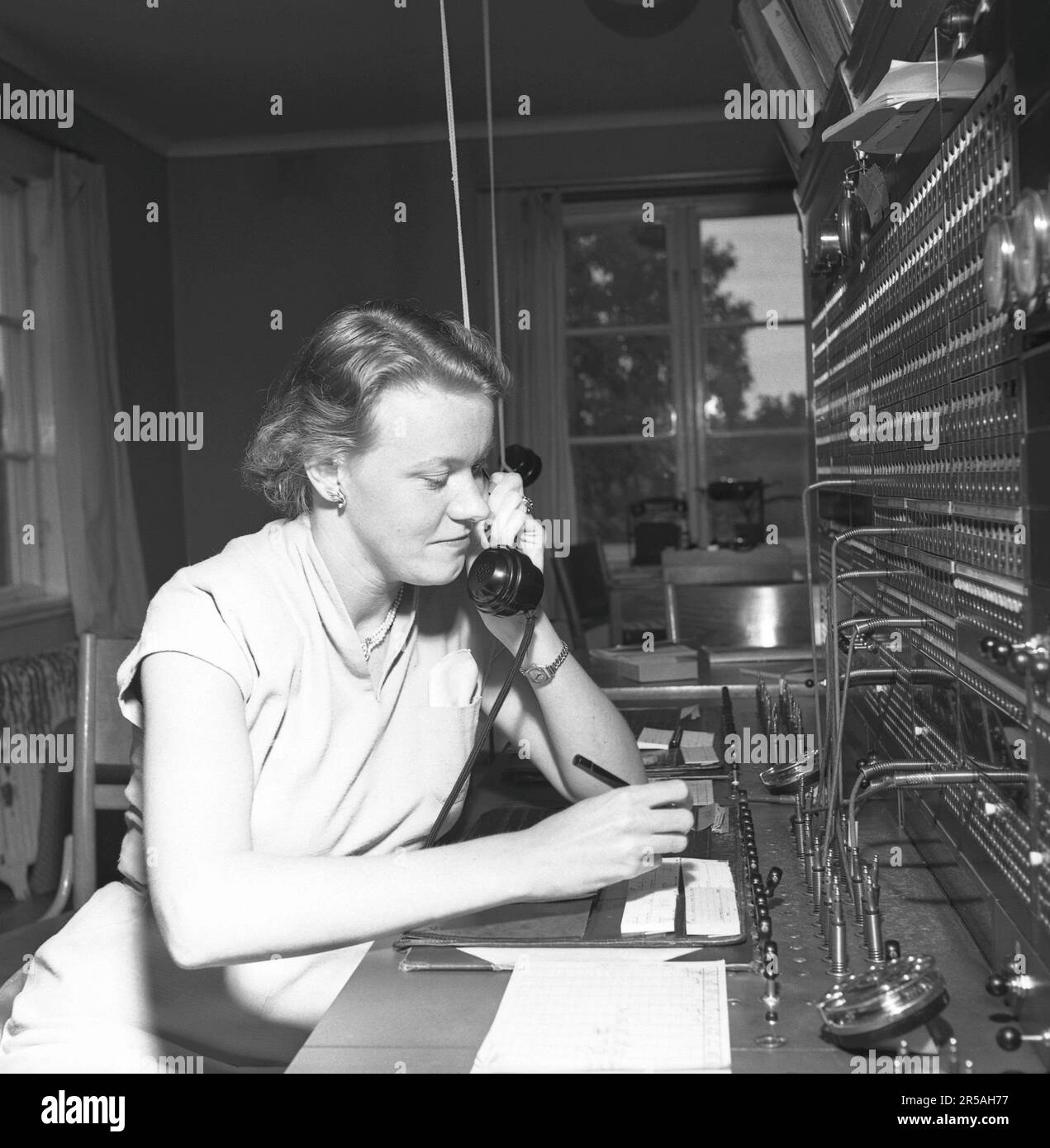 Telefonie in den 1950er. Eine Frau, die an einer Telefonzentrale arbeitet, als Vermittlung. Ein manuell betriebenes Telefonkommunikationssystem, bei dem die eingehenden Anrufe vom Betreiber weitergeleitet und an eine andere Telefonnummer umgeleitet wurden, in diesem Fall lokal innerhalb des Gebäudes, das ein Unternehmen oder eine Organisation mit vielen internen Telefonleitungen bedient. Die Telefonzentrale konnte Nachrichten entgegennehmen und Sie in die Warteschleife setzen, wenn die Leitung besetzt war. Schweden 1953. Conard Ref. 2489 Stockfoto