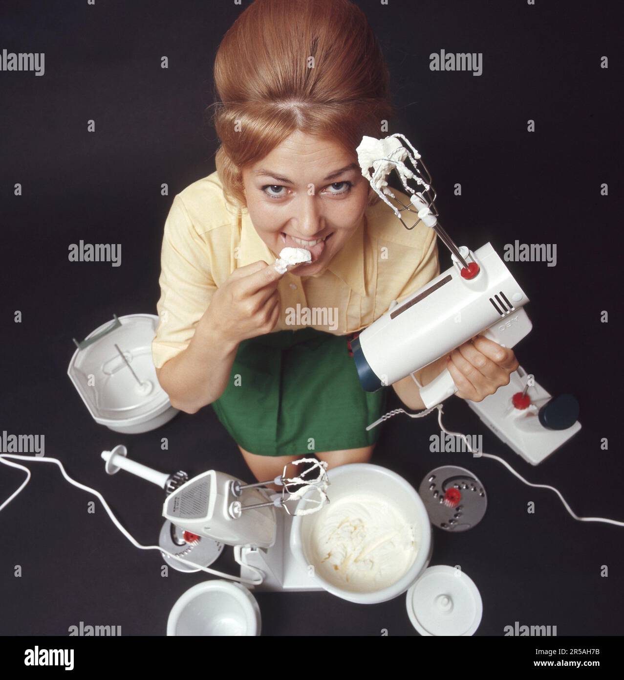 In den 1960er Jahren. Eine junge Frau mit einem elektrischen Mixer, die Schlagsahne hat und sie schmeckt. Sie trägt Kleidung in den typischen 1960er Farben und ihr Haar in der beliebten Beehive-Frisur. Schweden 1969. Kristoffersson Stockfoto