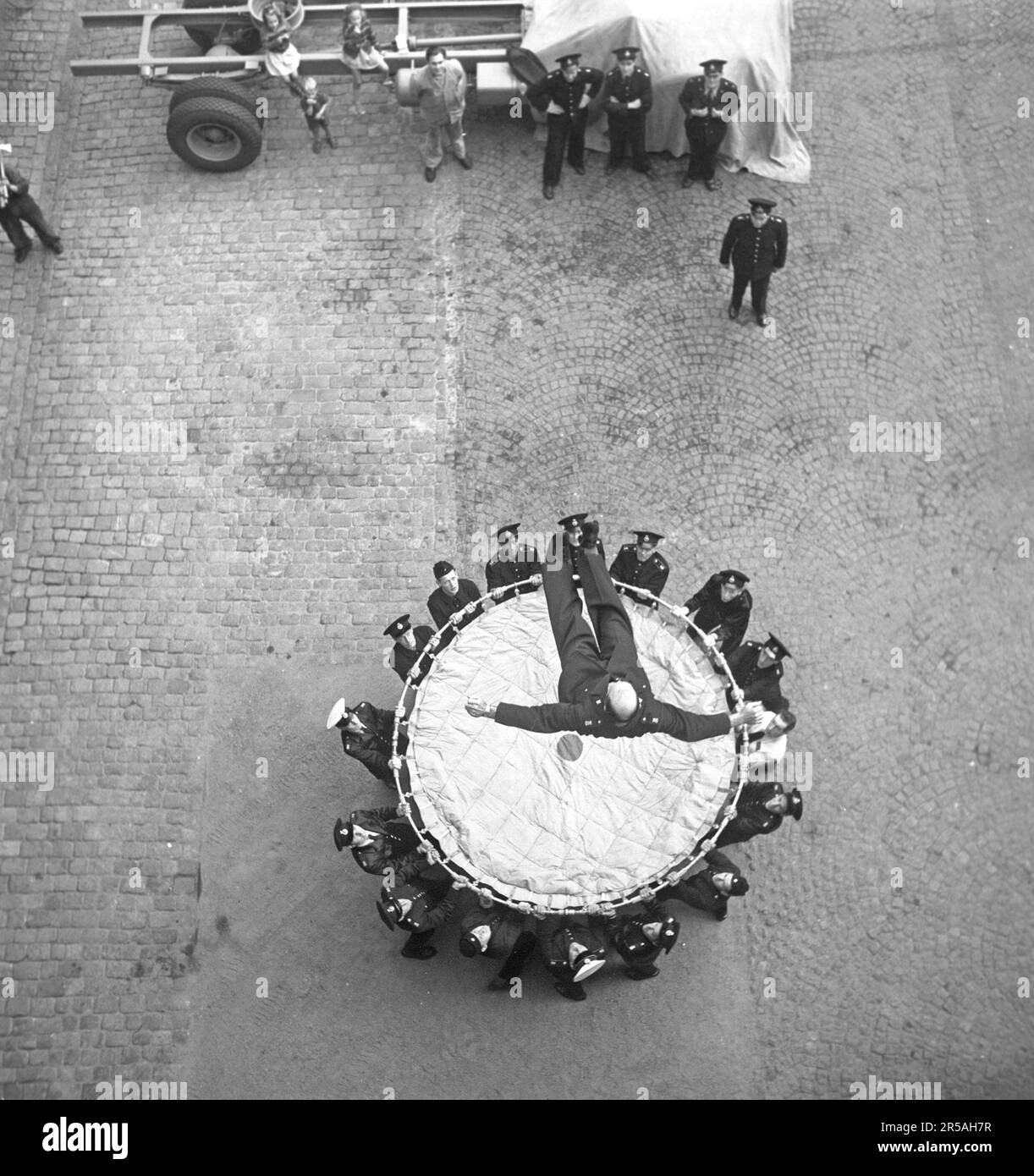 In den 1950er Jahren. Ein tapferer Feuerwehrmann landet in einem Lebensrettungsblatt. Ein Gerät, das 1887 erfunden wurde und bis in die 1980er Jahre verwendet wurde, um Menschen zu retten, indem sie sie von den oberen Stockwerken eines brennenden Gebäudes in das Netz springen ließen, in der Regel bis zum Boden. Die Feuerwehrleute glaubten, dass die praktische Höhenbegrenzung für die erfolgreiche Nutzung von Rettungsnetzen etwa sechs Stockwerke betrug, obwohl bei einem Brand in Chicago im Jahr 1930 drei Menschen Sprünge von einem achtstöckigen Gebäude in ein Rettungsnetz überlebten. Eine Übung irgendeiner Art und das Ereignis wird von oben fotografiert, kurz bevor er landet. Schweden 1952 Kristoffersson r Stockfoto