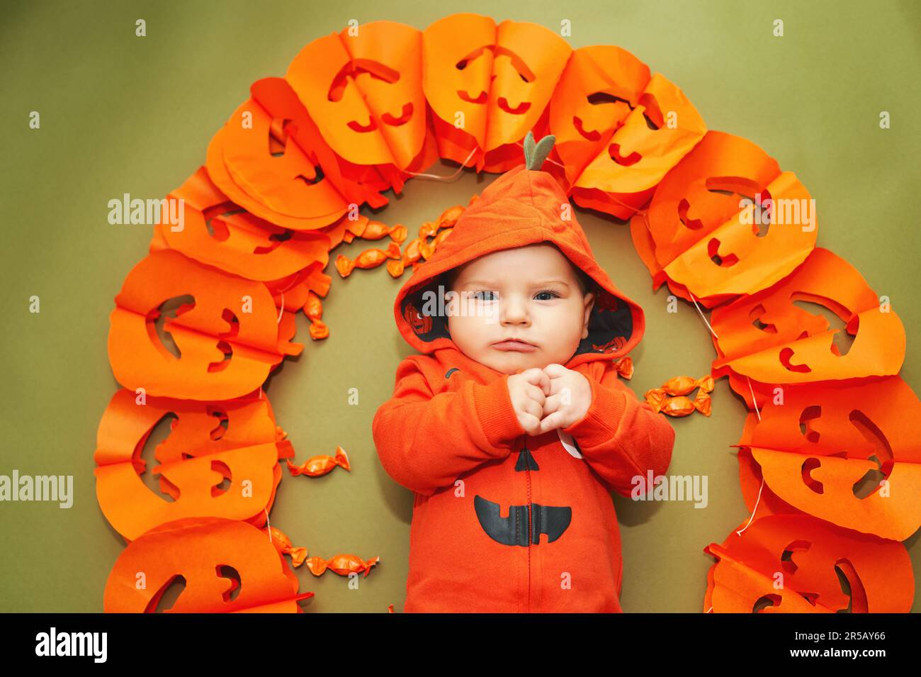 Halloween-Porträt eines niedlichen Babys, das auf grünem Hintergrund neben der Kürbis-Girlande liegt Stockfoto