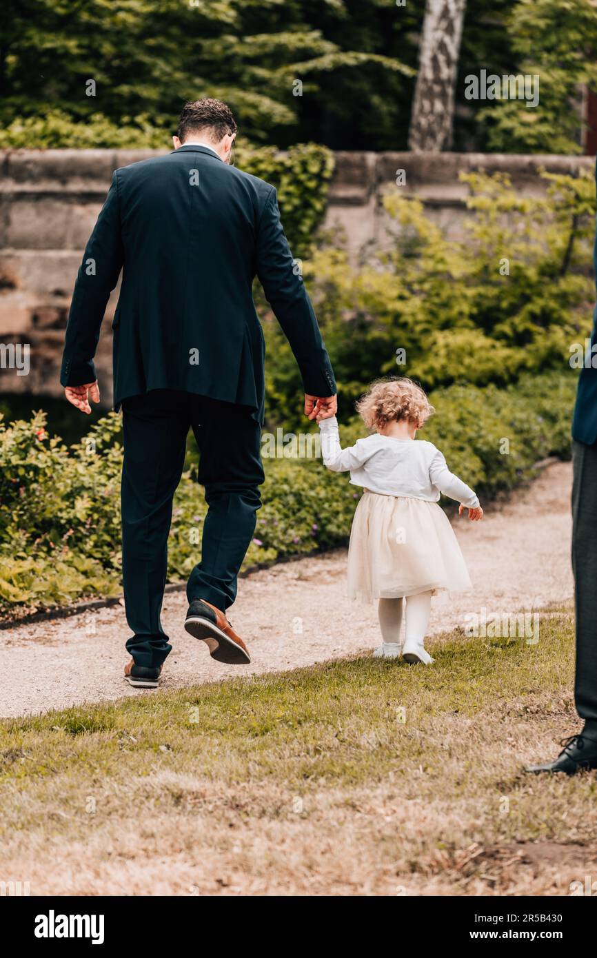 Ein vertikales Bild eines liebevollen Vaters, der mit seiner Tochter in formeller Kleidung in einem Park spaziert Stockfoto