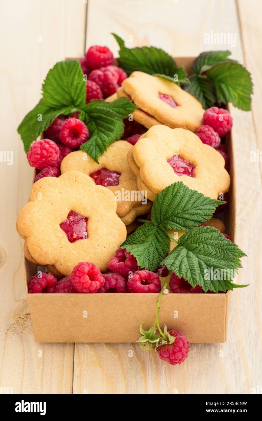 Hausgemachte Kekse mit Himbeermarmelade und frischen Himbeeren in einer handgefertigten Kiste auf Holzhintergrund. Stockfoto