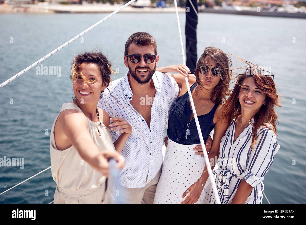 Eine Gruppe junger attraktiver Models macht ein Selfie auf dem Deck der Yacht, während sie an einem wunderschönen Sommertag am Meer durch die Anlegestelle reitet. S Stockfoto
