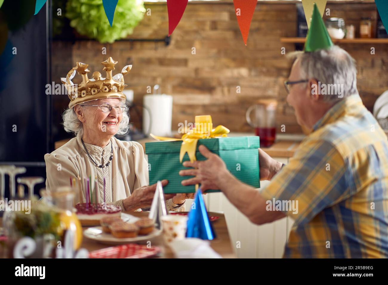 Schöne Geburtstagsfeier, während eine geliebte Oma von ihren Lieben umgeben ist. An diesem besonderen Tag schenkt ihr hingebungsvoller Opa ihr ein Du Stockfoto