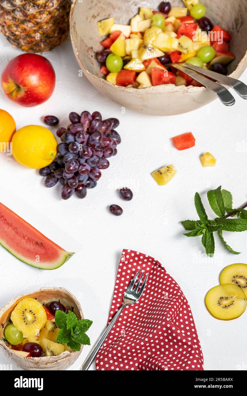 Frisch zubereiteter Obstsalat in einer großen, klassischen Schüssel und einer gefüllten Dessertschüssel. Mit Obst und Minze dekoriert. Stockfoto
