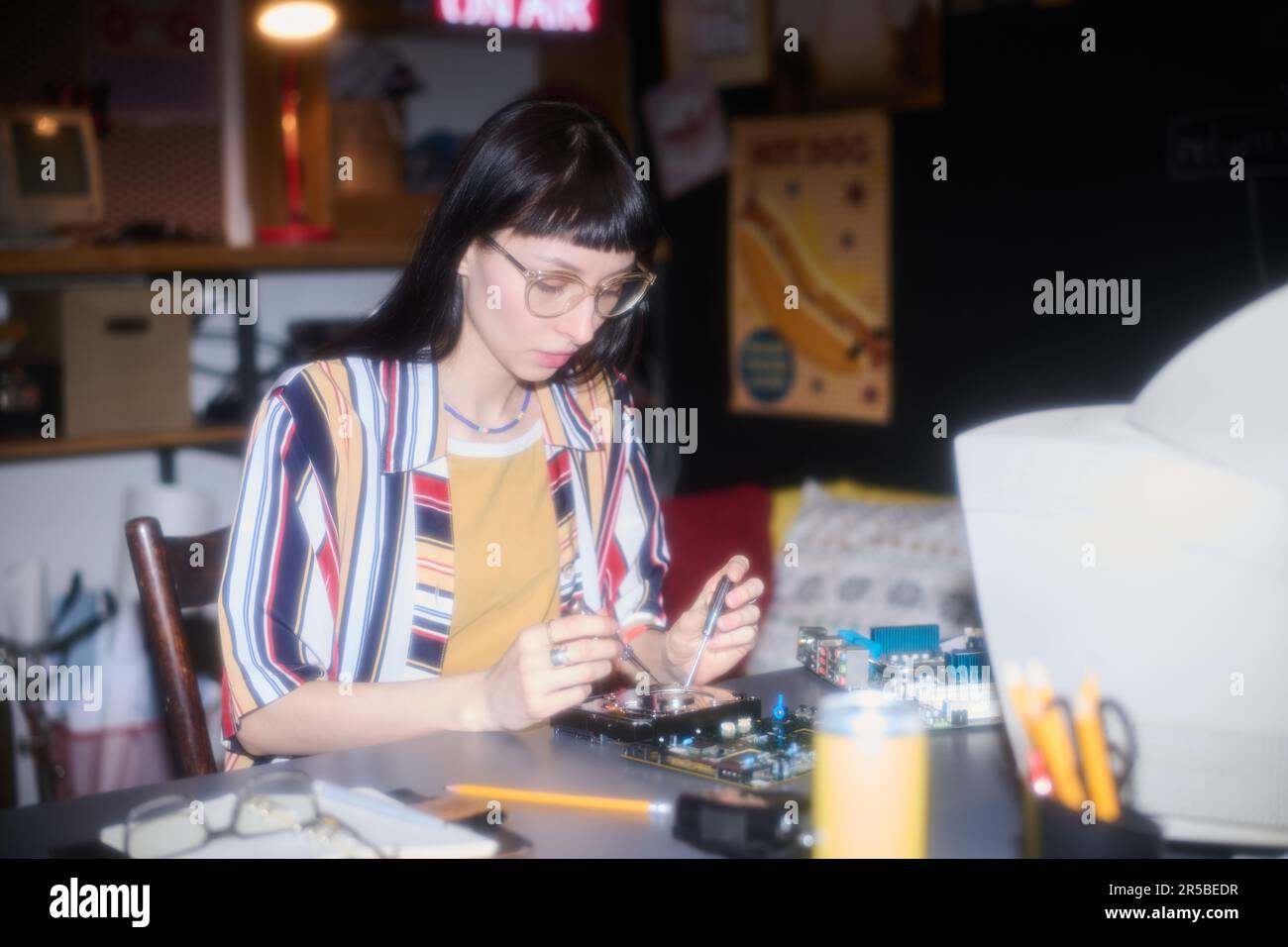 Konzentrierte junge Frau, die Arbeitsgeräte verwendet, während sie mit der Computerplatine am Tisch arbeitet Stockfoto