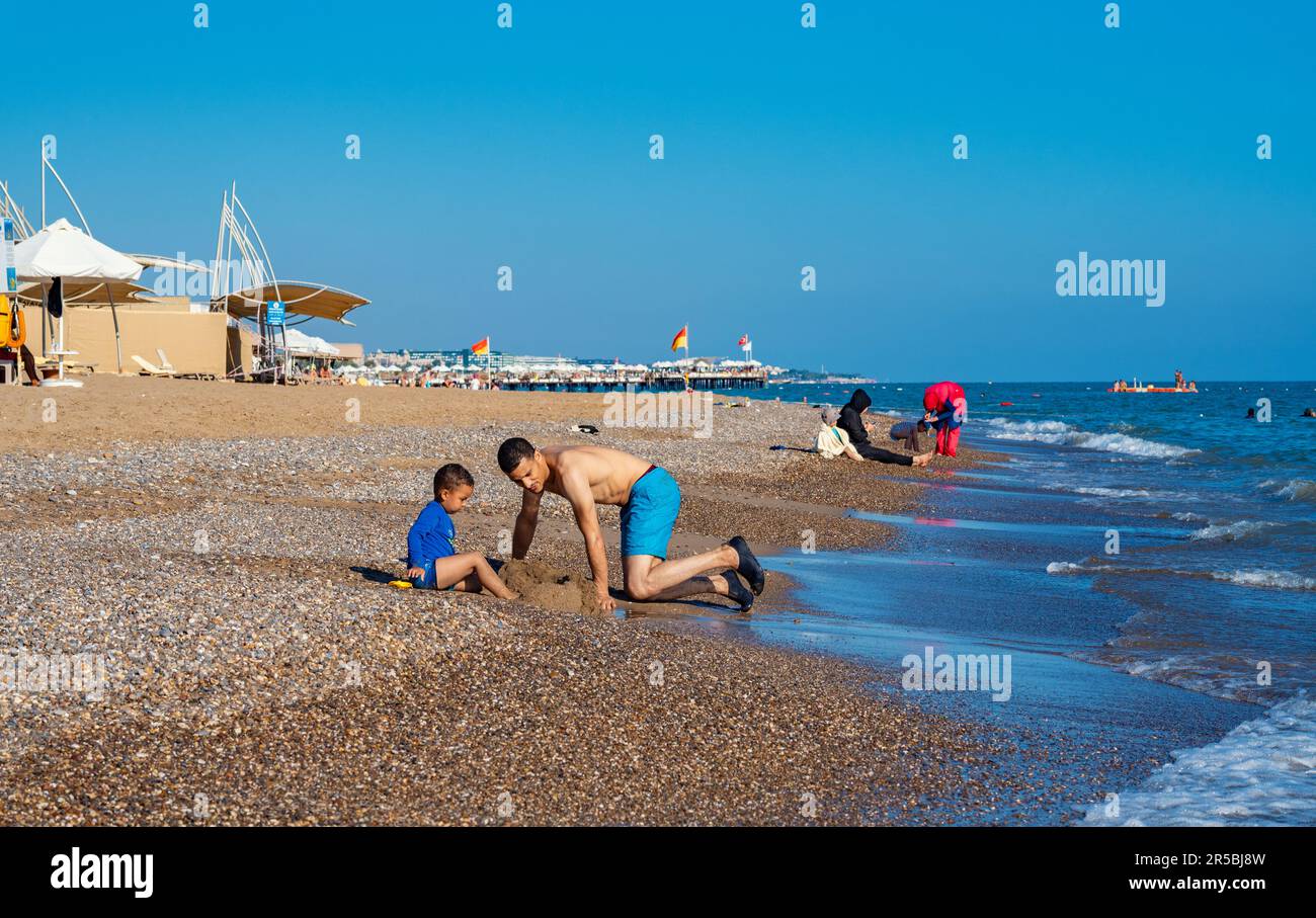 Antalya; Türkei-September 16; 2022: Ein junger Mann, der mit seinem Jungen eine Sandburg am Meer baut. Menschen, die sich sonnen, schwimmen oder auf der Straße laufen Stockfoto