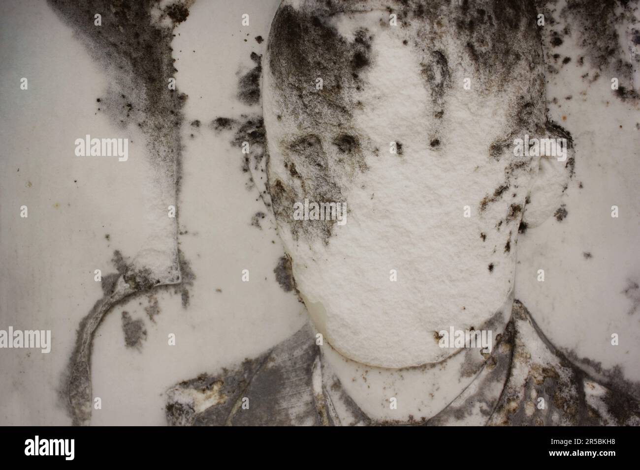 Das abgenutzte und verwitterte, kaum erkennbare Gesicht einer Person, die in eine natürliche Steinmauer geschnitzt wurde. Stockfoto