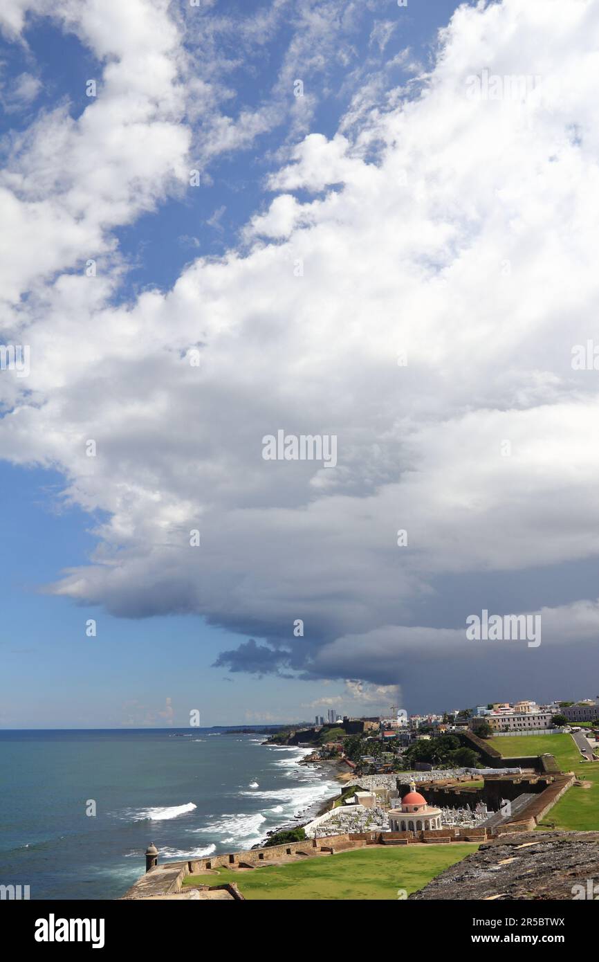 Ein malerischer Blick auf eine Meeresklippe mit mehreren Häusern im Hintergrund, vor dem Hintergrund eines weiten blauen Himmels mit weißen Wolken Stockfoto