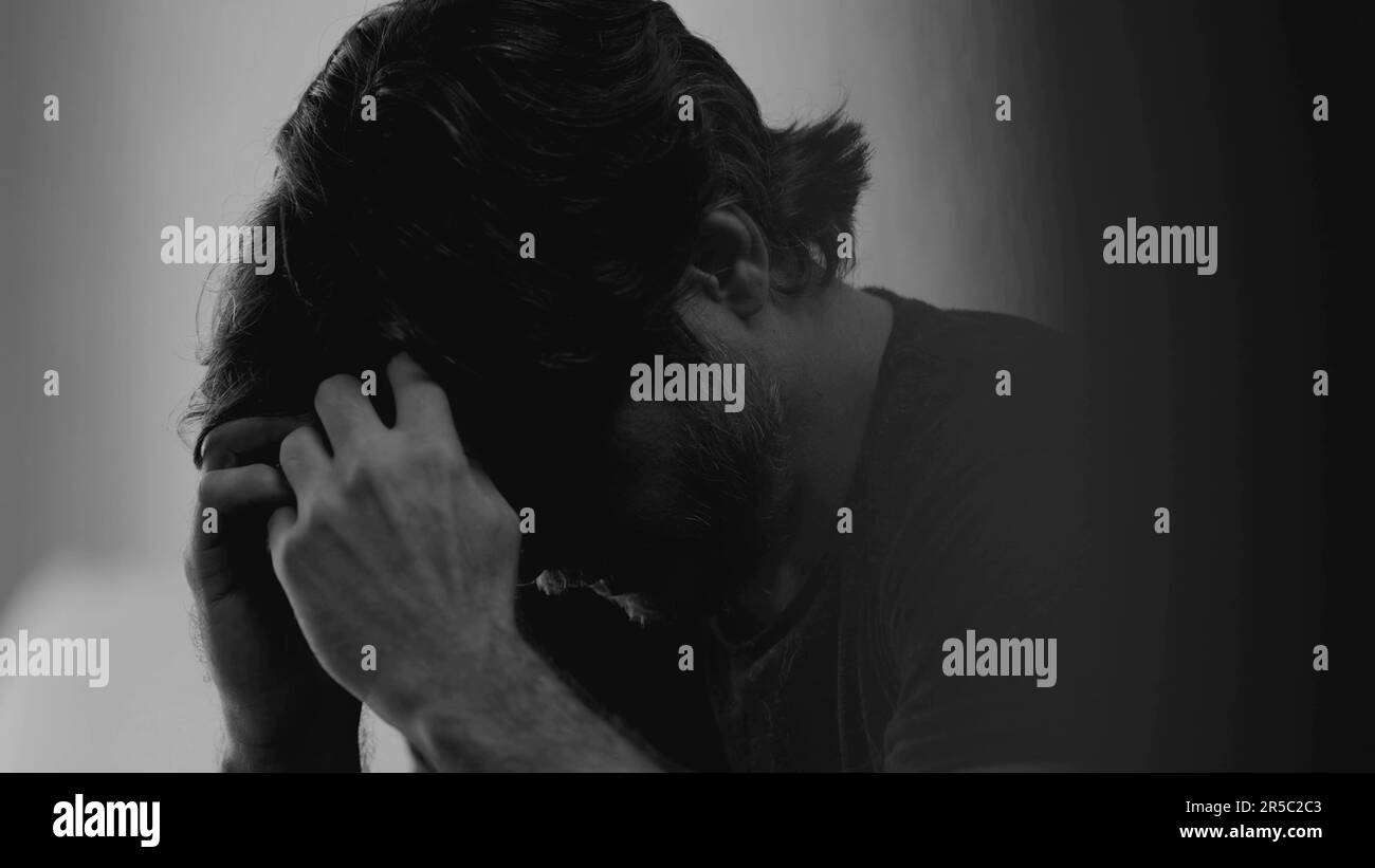Dramatisch depressiver junger Mann mit emotionalem Schmerz. Düsteres Nahtgesicht eines Mannes in 30s Jahren, der Traurigkeit empfindet und sich in monochromatischem Schwarz verirrt hat Stockfoto