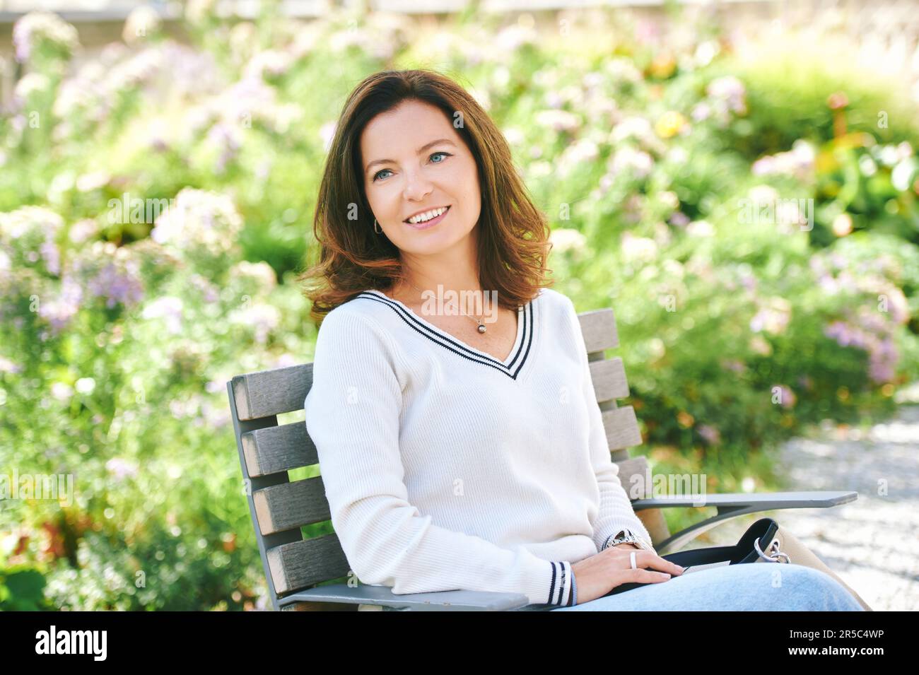 Außenporträt einer wunderschönen 40 - 45 Jahre alten Frau, die auf einer Bank im grünen Park sitzt, gesunder Lebensstil Stockfoto