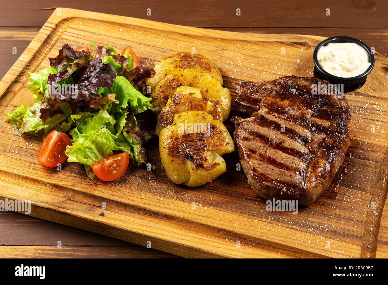 Gegrillter Rib Eye Black Angus mit Pommes Frites, grünem Salat und Sauce auf Holzhintergrund. Stockfoto