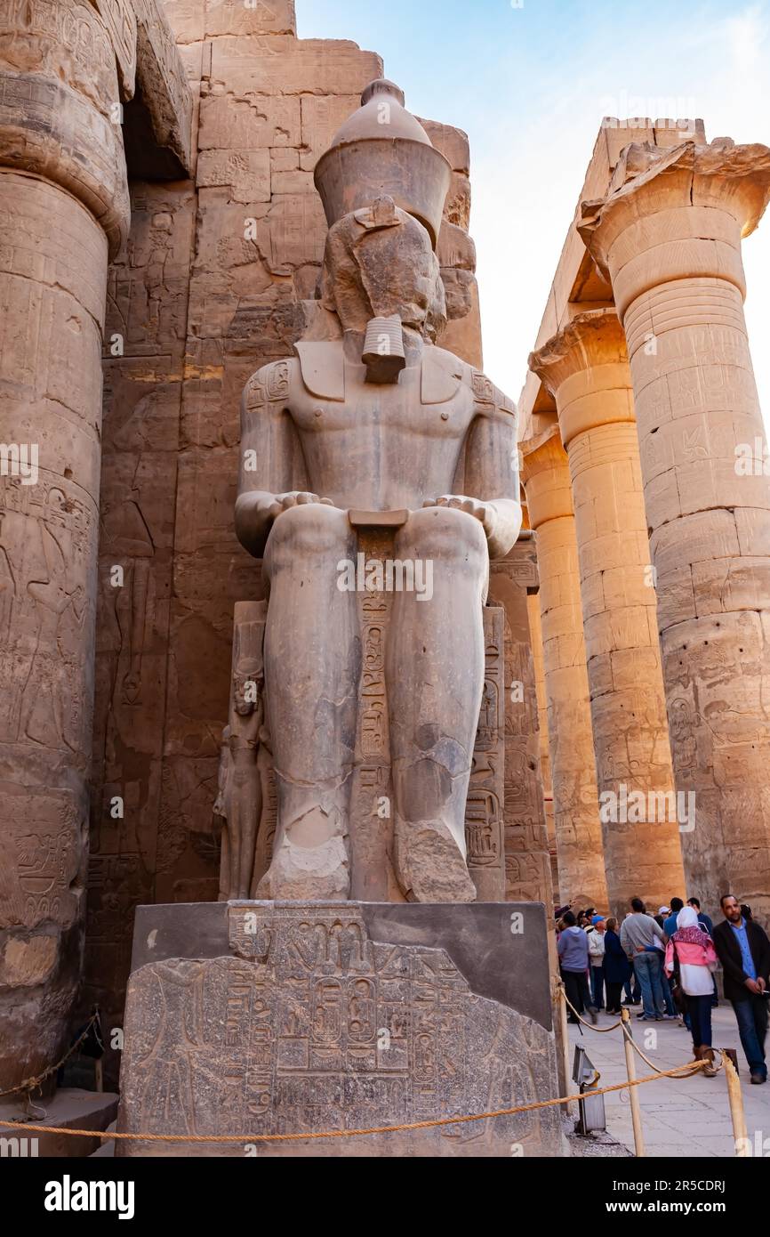 Luxor, Ägypten - 2. Januar 2012 : Statue des Pharaos Ramses II mit der großen Kolonnade und unbekannten Touristen, die im Tempel von Luxor, Luxor, Ägypten, spazieren gehen Stockfoto