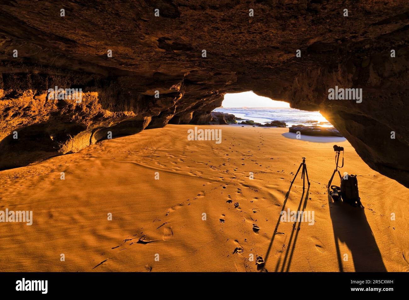 Im Inneren einer malerischen Sandsteinklippen-Meereshöhle an der Pazifikküste Australiens bei Sonnenaufgang mit Fotokamera auf dem Stativ. Stockfoto