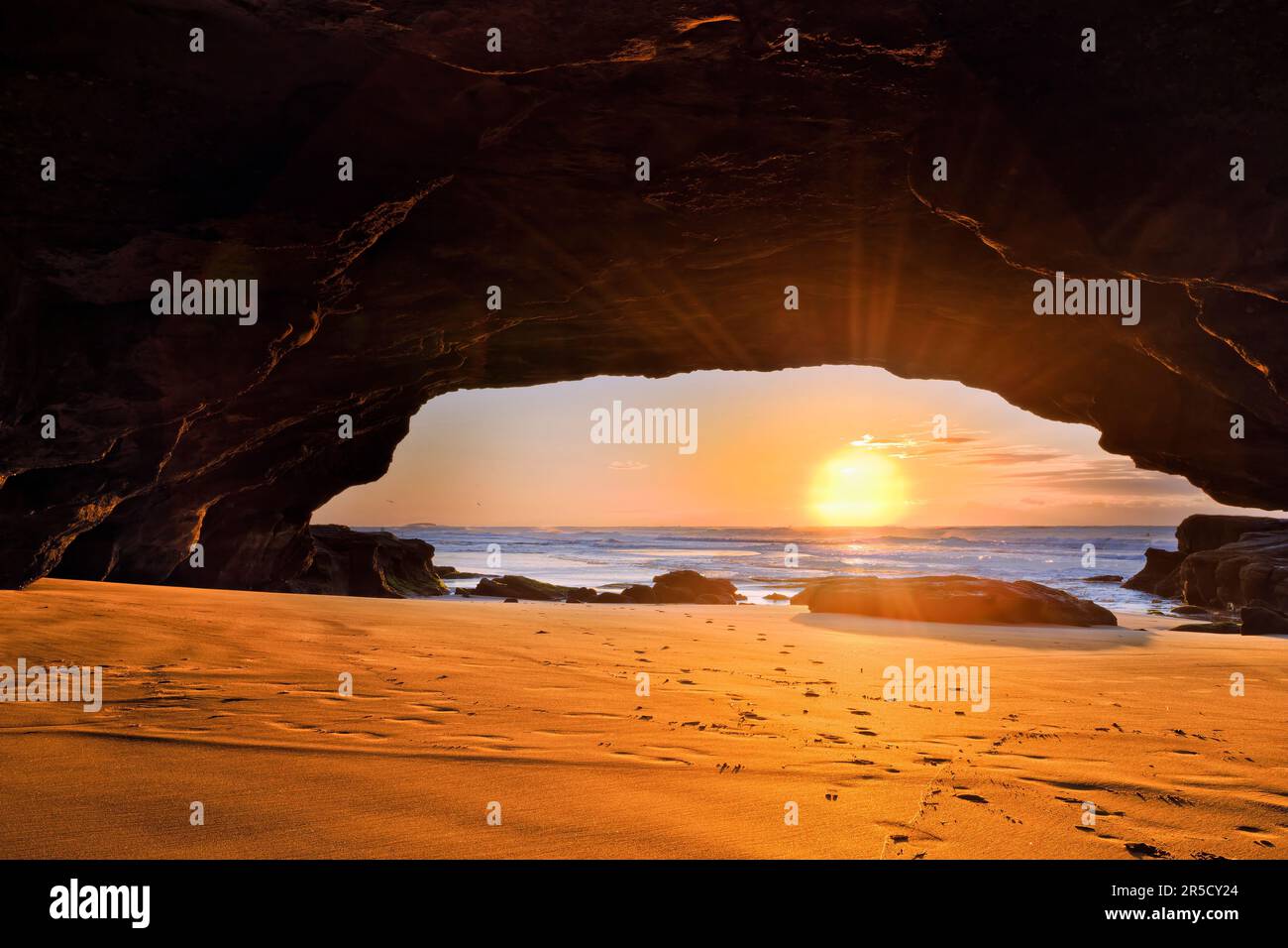 Im Inneren der malerischen Meereshöhle an der Pazifikküste Australiens bei Caves Beach Town mit aufgehender Sonne. Stockfoto