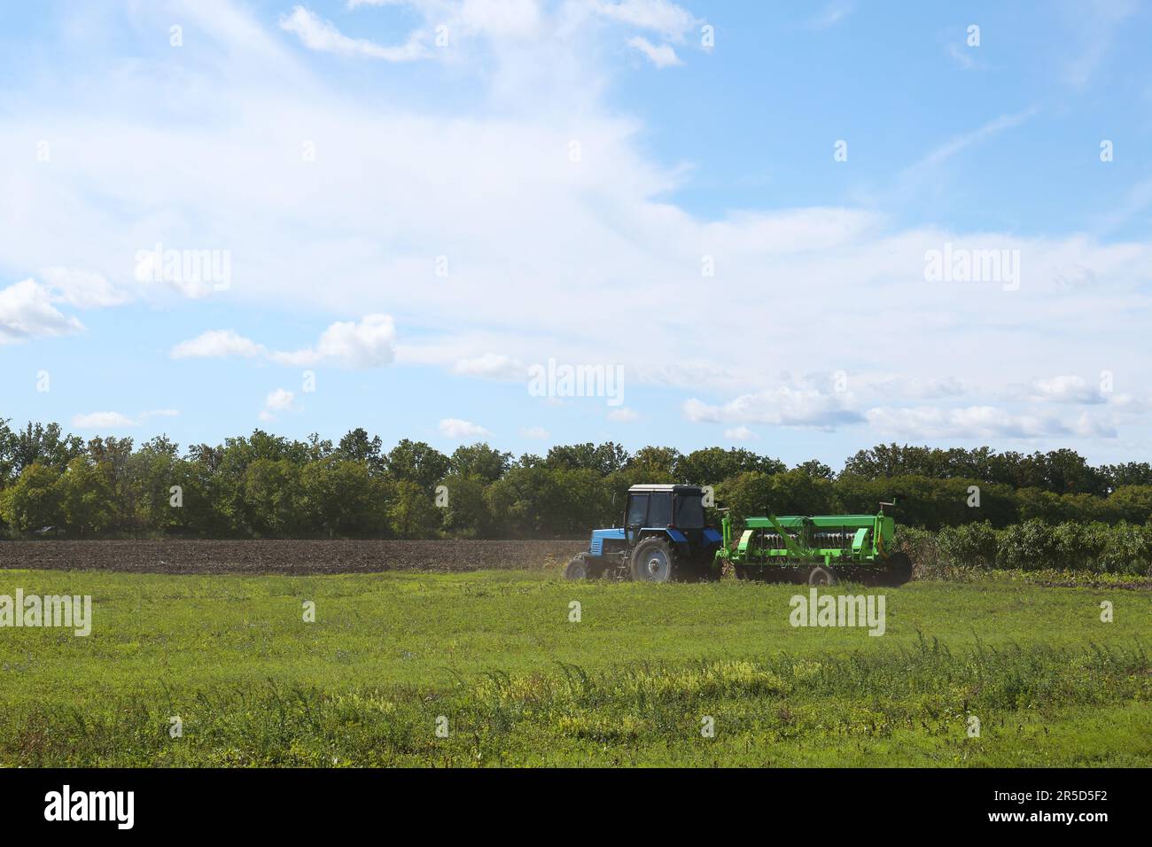 Moderne Traktor-Erntemaschine auf dem landwirtschaftlichen Feld an sonnigen Tagen Stockfoto