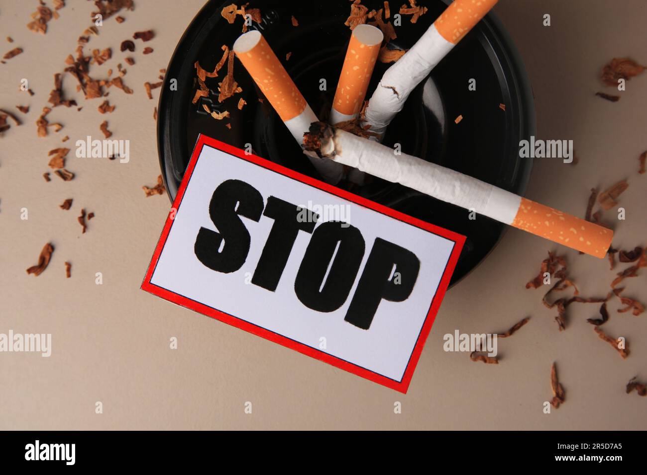 Karte mit Wort Stopp, Aschenbecher und Zigarettenstummel auf beigefarbenem Hintergrund, flach gelegt. Raucherentwöhnungskonzept Stockfoto