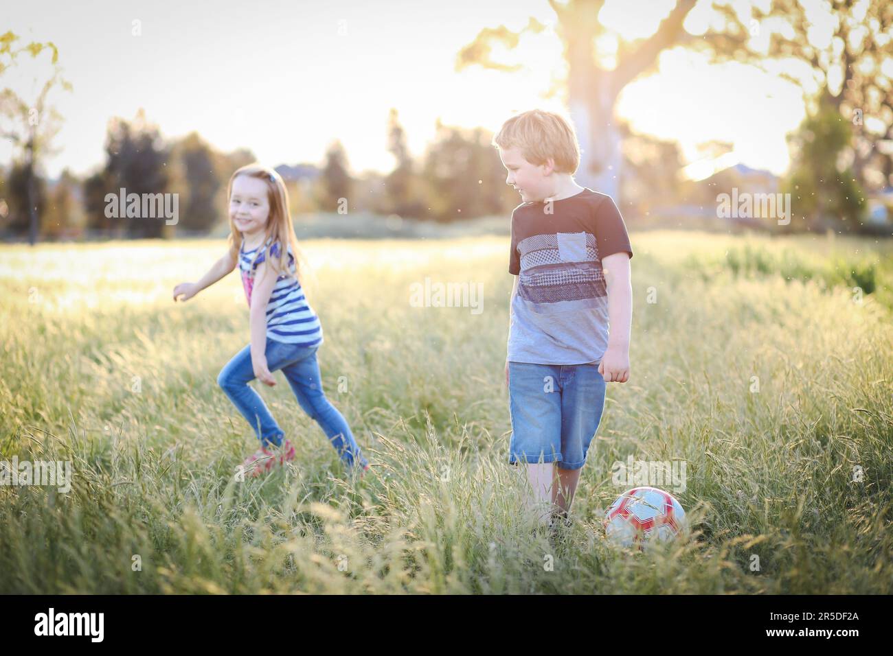 Junge und Mädchen Rennen durch langes Gras und spielen Fußball im Park. Australische Kinder haben Spaß im Freien in der Natur Stockfoto