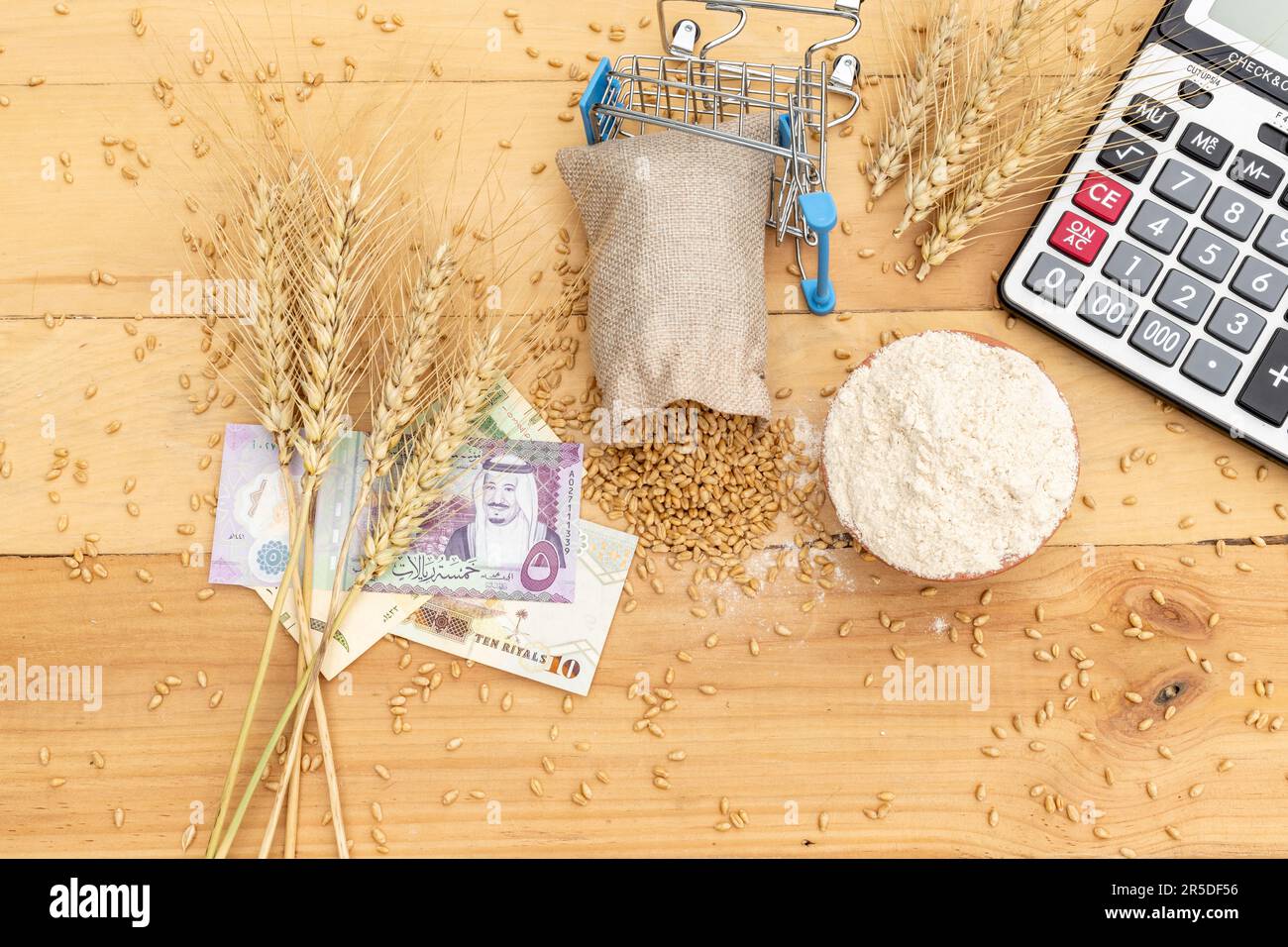 Weizenzapfen auf saudischem Rial mit Weizenkörnern und Mehl auf Holzhintergrund. Weizenpreiskonzept Stockfoto