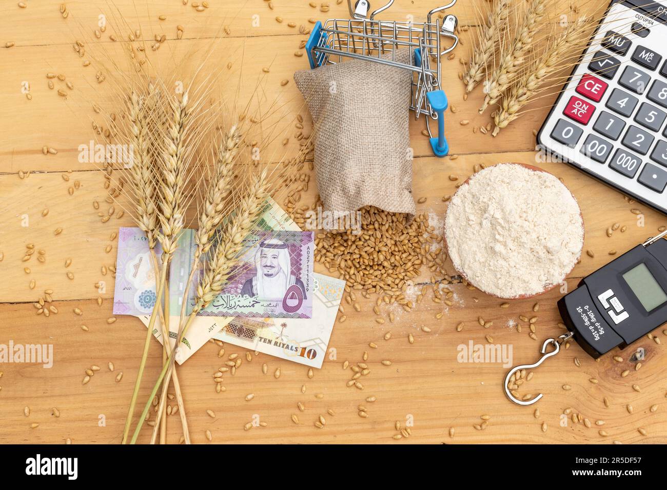 Weizenzapfen auf saudischem Rial mit Weizenkörnern und Mehl auf Holzhintergrund. Weizenpreiskonzept Stockfoto