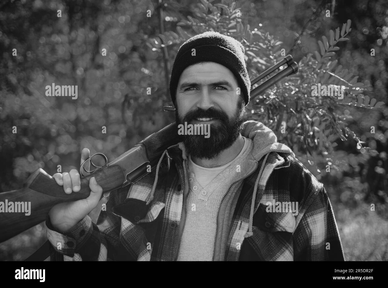 Ein bärtiger Jäger, der eine Waffe in der Hand hält und im Wald herumläuft. Jäger mit Schrotflinte auf der Jagd. Die Jagdsaison im Herbst Stockfoto