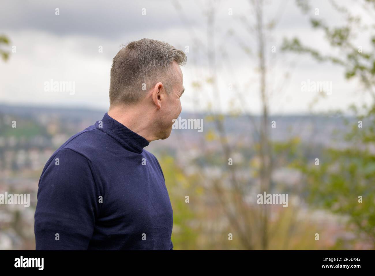 Ein Mann mit grauhaarigen Haaren im blauen Pullover steht auf einem Berg und schaut nach hinten Stockfoto