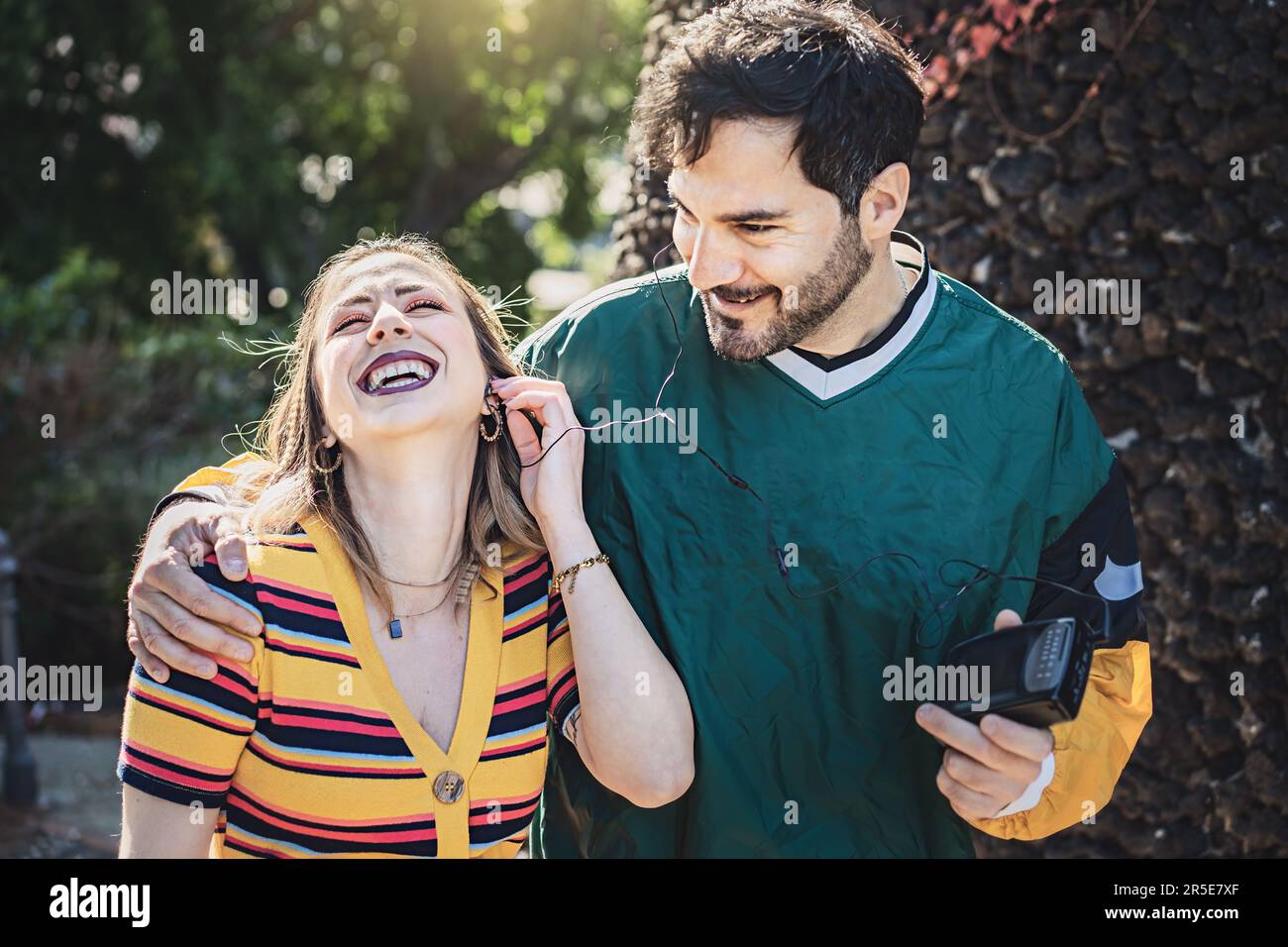 Eine ehrliche Aufnahme eines jungen Mannes und einer jungen Frau, die an einem sonnigen Tag im Park spazieren und die 90s mit einem Kassettenrekorder wiedererleben. Sie teilen sich ein Paar Ohrhörer Stockfoto