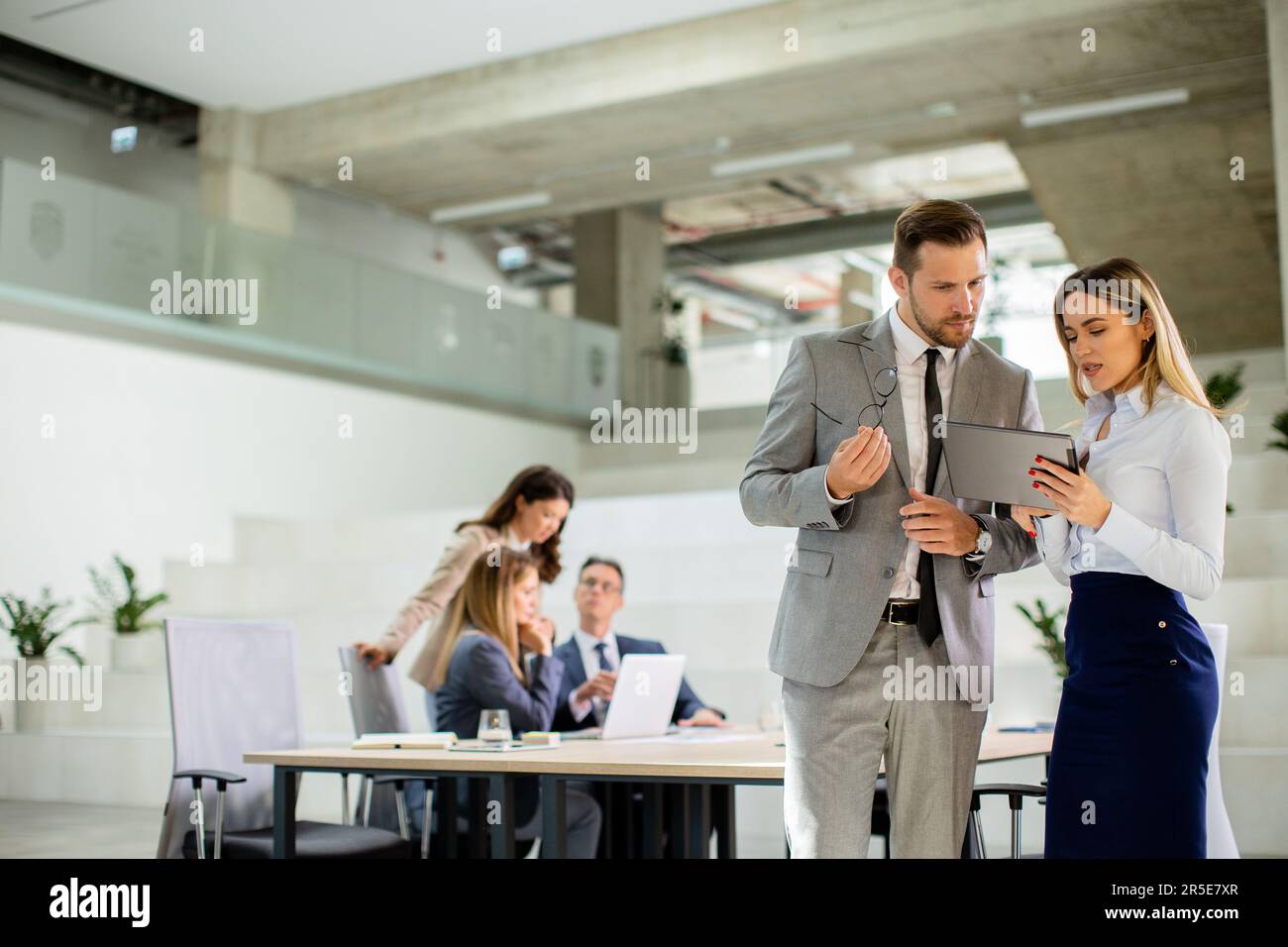 Attraktives junges Geschäftspaar, das sich die finanziellen Ergebnisse auf einem digitalen Tablet vor seinem Team im Büro ansieht Stockfoto